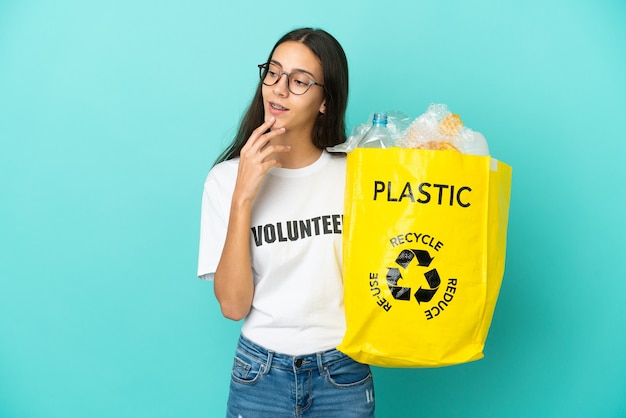 Jovem francesa segurando uma sacola cheia de garrafas plásticas para reciclar, olhando para cima enquanto sorri