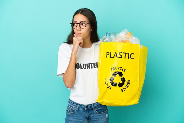 Jovem francesa segurando uma sacola cheia de garrafas plásticas para reciclar, tendo dúvidas e pensando