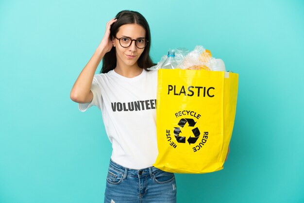 Jovem francesa segurando uma sacola cheia de garrafas plásticas para reciclar, tendo dúvidas