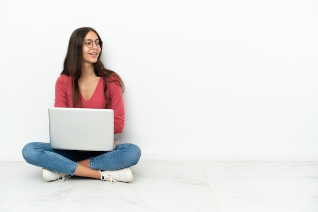 Jovem francesa sentada no chão com o laptop na posição lateral