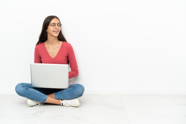 Jovem francesa sentada no chão com seu laptop olhando de lado