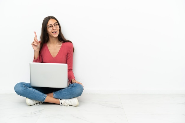 Jovem francesa sentada no chão com seu laptop tentando descobrir a solução enquanto levanta um dedo