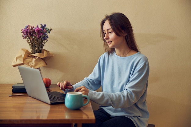 Jovem freelancer alegre, confiante e feliz trabalhando em um laptop na cozinha de casa