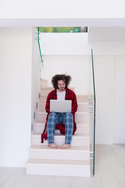 Foto jovem freelancer em roupão trabalhando em casa usando o laptop enquanto está sentado na escada