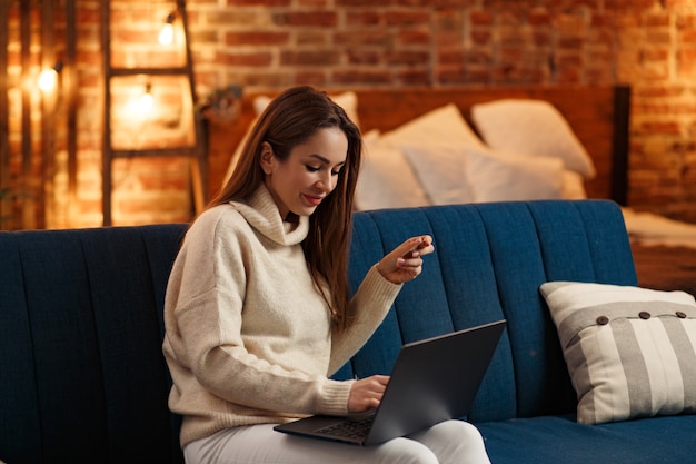 Jovem freelancer em um escritório em casa segurando um cartão de crédito e usando um laptop