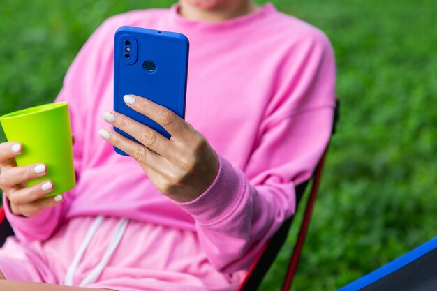 Jovem freelancer feminina toda rosa sentada em uma cadeira ao ar livre relaxando usando smartphone para trabalhar O conceito de trabalho remoto