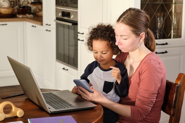 Jovem freelancer feminino com filho pequeno fofo e smartphone