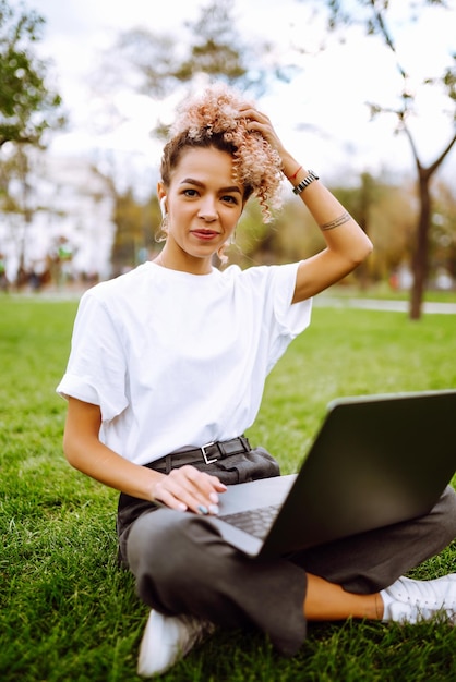 Jovem freelancer gostando de assistir webinar educacional no laptop sentado na grama verde