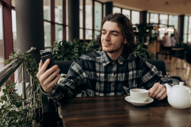 Jovem freelancer masculino tirando uma selfie em um café aconchegante