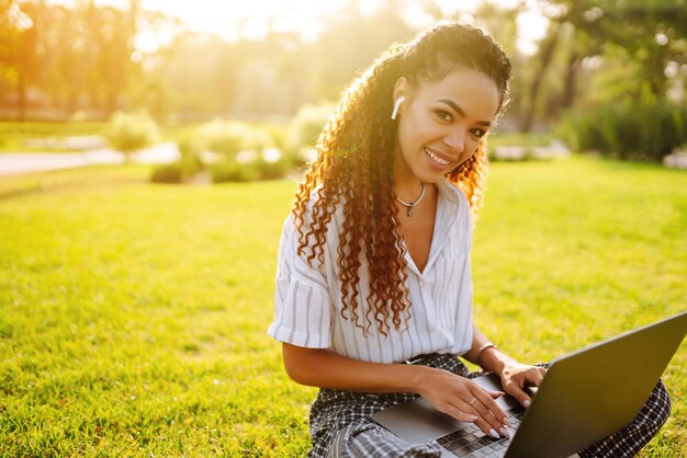 Jovem freelancer sentada em grama verde com laptop Educação on-line