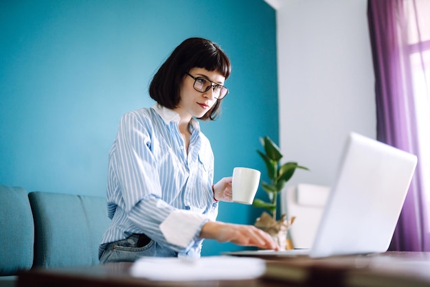 Jovem freelancer sentada no sofá moderno e trabalhando no laptop Educação on-line Trabalhando em casa