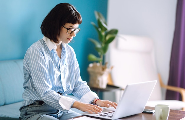 Jovem freelancer sentada no sofá moderno e trabalhando no laptop Educação on-line Trabalhando em casa