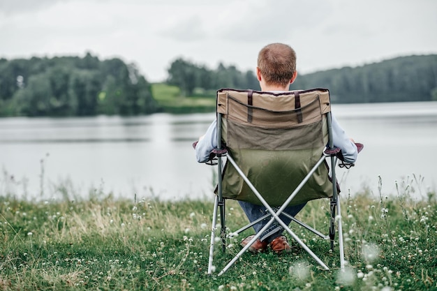 Jovem freelancer sentado na cadeira e relaxando na natureza perto do lago Atividade ao ar livre no verão Aventura viajando no parque nacional lazer férias relaxamento