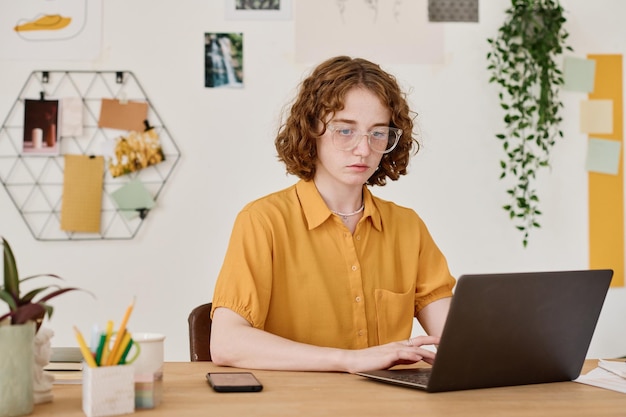 Jovem freelancer sério em rede de camisa e óculos em home office