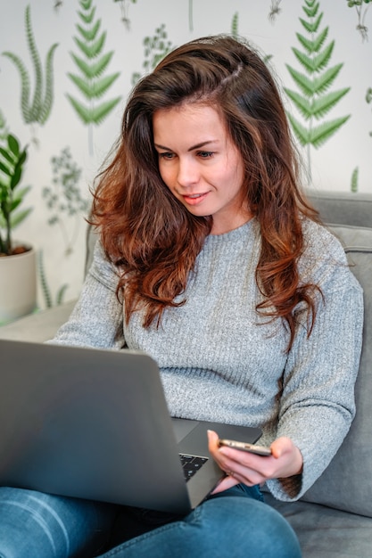 Jovem freelancer sorridente, sentada no sofá, aproveitando o trabalho remoto de casa