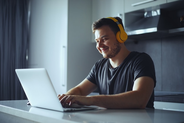 Jovem freelancer sorridente usando laptop, estudando online e trabalhando em casa