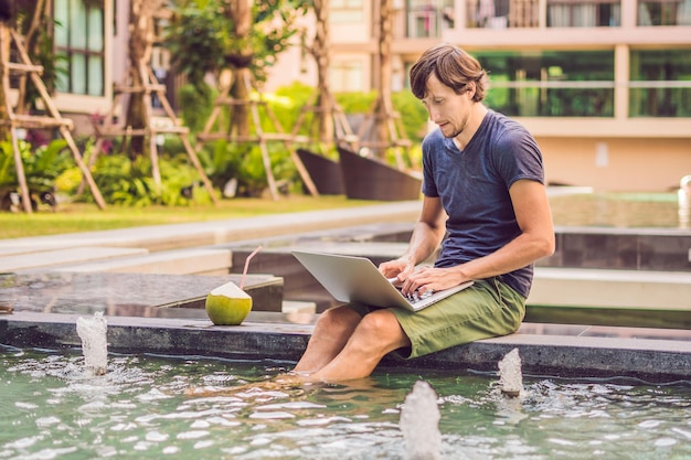 Jovem freelancer trabalhando de férias à beira da piscina.