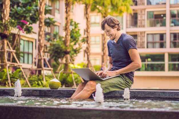 Jovem freelancer trabalhando de férias ao lado da piscina