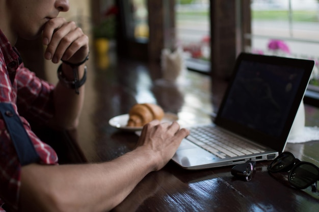 Jovem freelancer trabalhando em um café com um laptop hipster usando um laptop moderno enquanto trabalhava em um loft vintage closeup de mãos masculinas