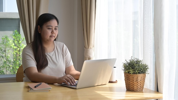 Jovem freelancer trabalhando on-line verificando e-mails em seu laptop pela manhã