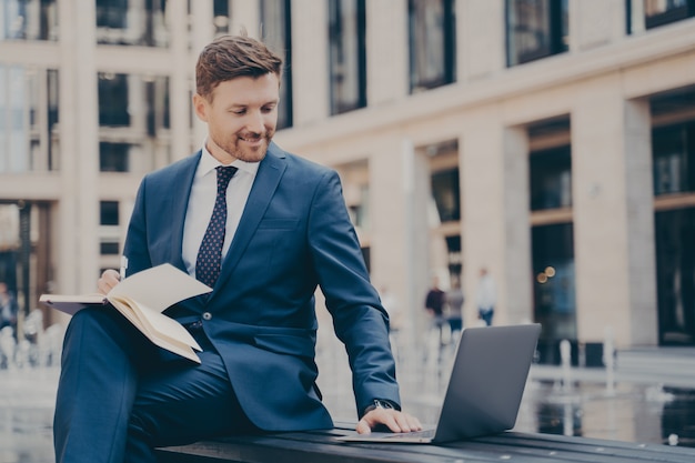 Jovem funcionário profissional de uma empresa pesquisando em um laptop ou assistindo a um webinar de negócios ao ar livre