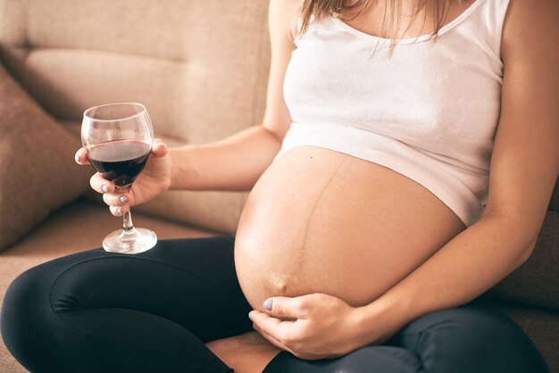 Jovem futura mãe sentada em casa bebendo álcool