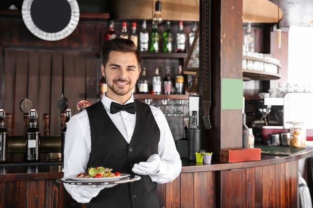 Jovem garçom com salada em restaurante