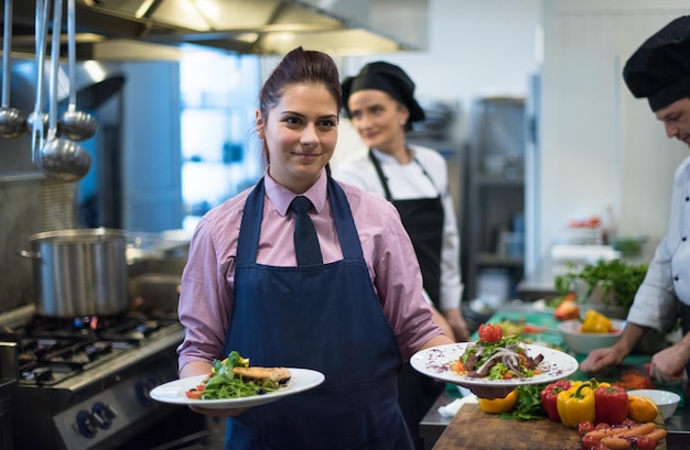 Jovem garçonete apresentando pratos de comidas saborosas em cozinha comercial