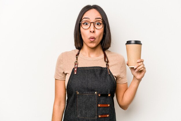 Jovem garçonete caucasiana segurando café isolado no fundo branco encolhe os ombros e abre os olhos confusos