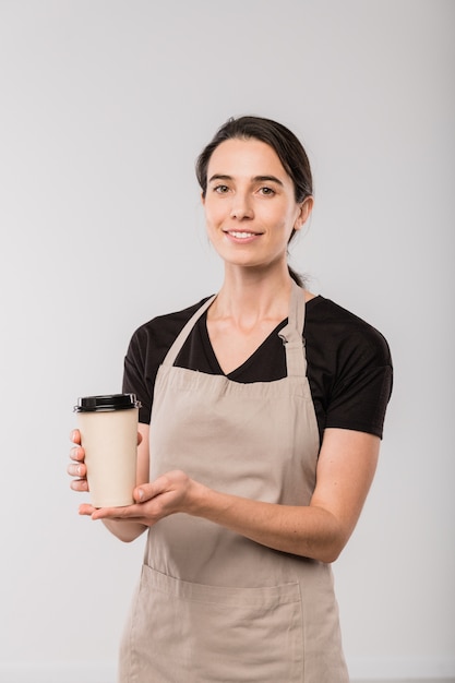 Jovem garçonete de café de avental dando a você um copo de café quente enquanto fica isolado na frente da câmera