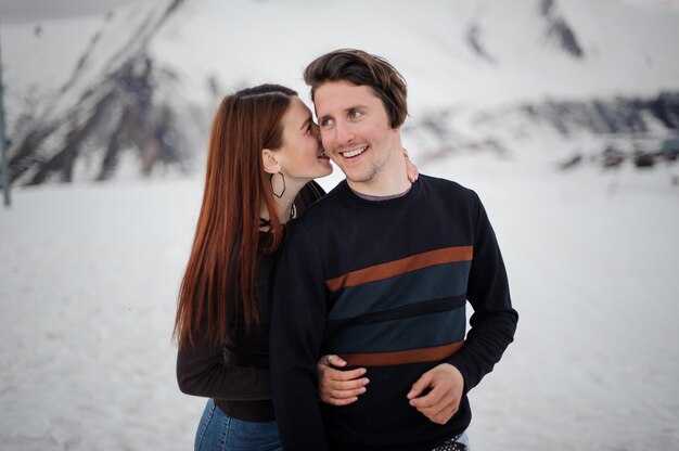 Jovem garota abraçando e beijando o namorado de volta na montanha de neve