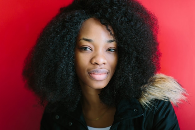 Jovem garota afro-americana linda com um casaco preto, sorrindo em fundo vermelho