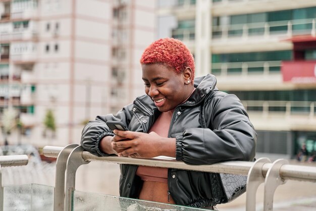 Jovem garota afro-americana sorrindo usando seu celular na cidade