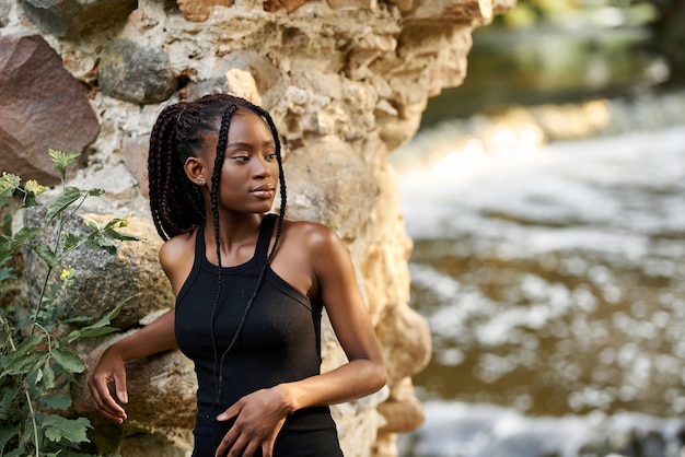 Foto jovem garota afro deslumbrante em um vestido preto de verão posando nas ruínas da floresta