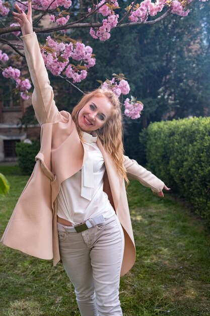 Jovem garota alegre caminha na primavera florecendo parque se diverte e dança jovem mulher atraente ao ar livre quadro vertical