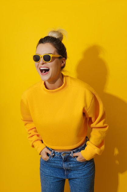 Foto jovem garota alegre vestindo camisola amarela e óculos de sol contra fundo amarelo