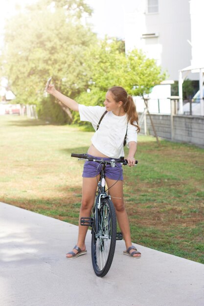 Foto jovem garota andando de bicicleta no parque e tirando uma selfie