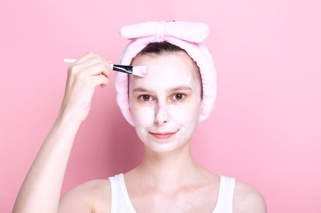 Jovem garota aplica máscara cosmética com pincel. Dia de spa conceito em casa, descanso e relaxamento