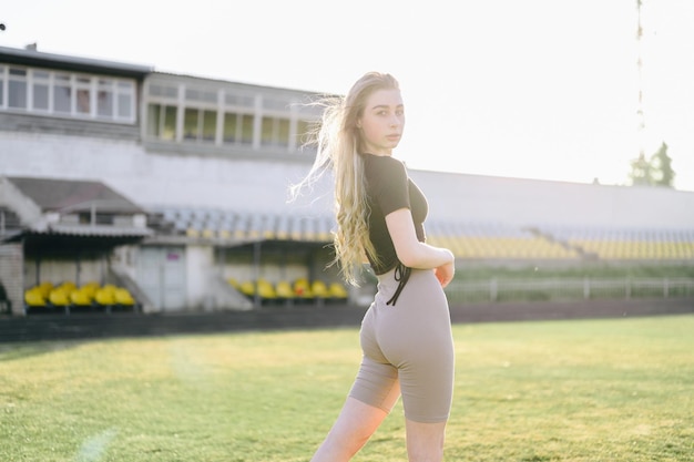 Jovem garota atlética posando no estádio ao pôr do sol Jovem em roupas esportivas Cabelo se desenvolve no vento