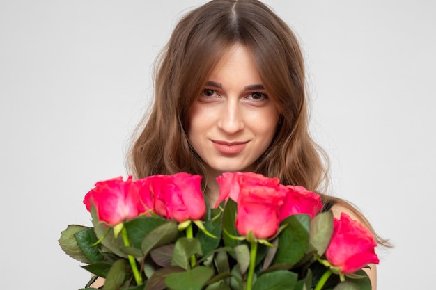 Jovem garota atraente com um buquê de rosas vermelhas em um fundo branco Uma garota feliz com um buquê de rosas está sorrindo O conceito de felicidade, alegria e celebração