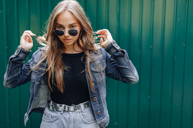 Jovem garota atraente em roupas jeans em copos em um simples fundo verde escuro com lugar para texto.