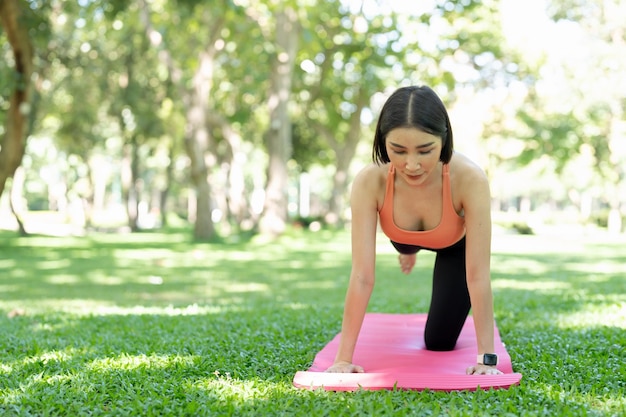 Jovem garota atraente está fazendo yoga asana avançado na esteira de fitness no meio de um parque