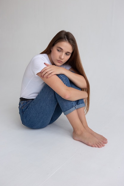 Jovem garota bonita caucasiana com cabelo comprido em camiseta, jeans azul no estúdio