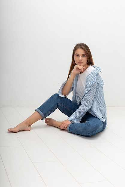 Jovem garota bonita caucasiana com cabelo comprido na camisa, jeans azul sentada no estúdio
