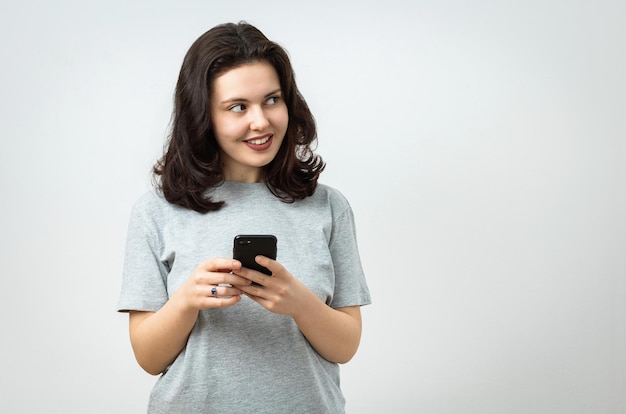 Jovem garota bonita e alegre segurando um celular e olhando para o espaço de cópia