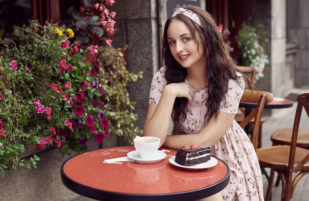 Jovem garota brilhante linda em um vestido de verão, sentado em uma mesa de café europeu