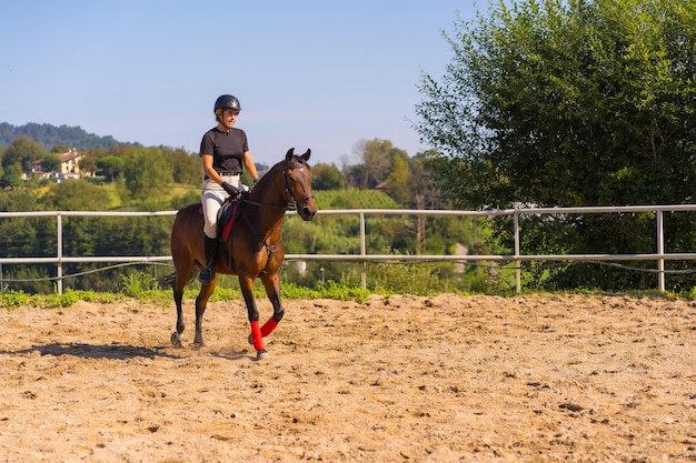 Jovem garota caucasiana cavalgando a cavalo com um cavalo marrom, vestida de cavaleiro preto com chapéu de segurança