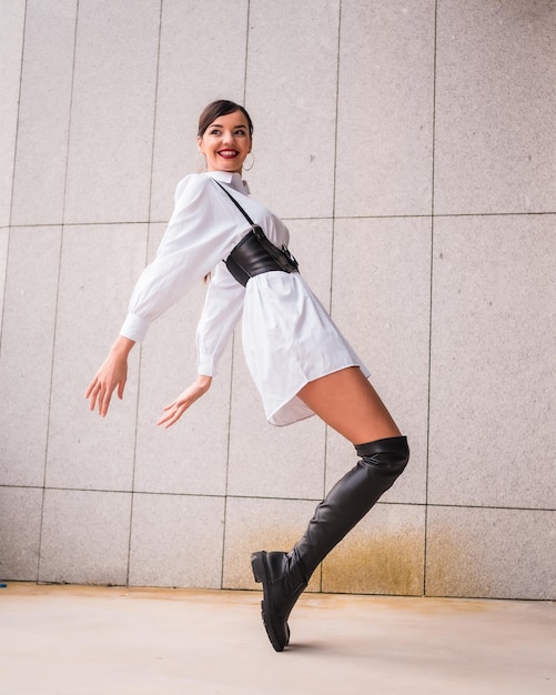 Jovem garota caucasiana com camisa branca e botas de couro preto Desfrutando de férias na cidade elevada posando na moda