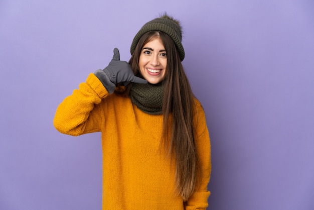 Jovem garota caucasiana com chapéu de inverno isolado na parede roxa, fazendo gesto de telefone. ligue-me de volta sinal