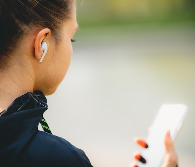 Jovem garota caucasiana com fones de ouvido sem fio no parque usando tablet e sorrindo